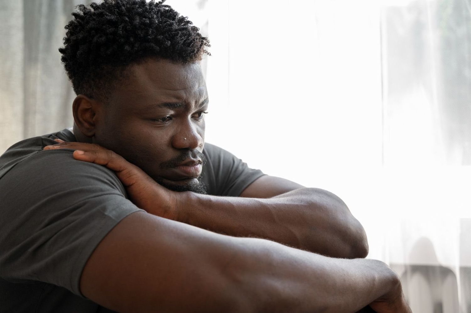 A man is sitting on a couch looking out a window.